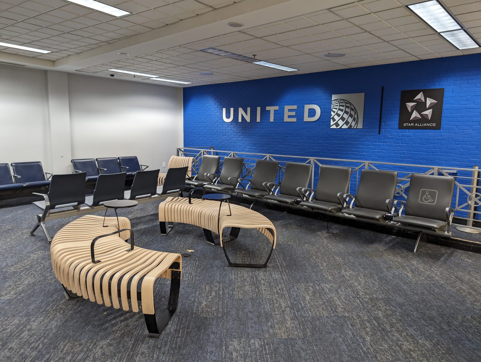 Interior photograph of a United Airlines gate seating area in Concourse C with rows of seats, windows onto the apron, and overhead signage