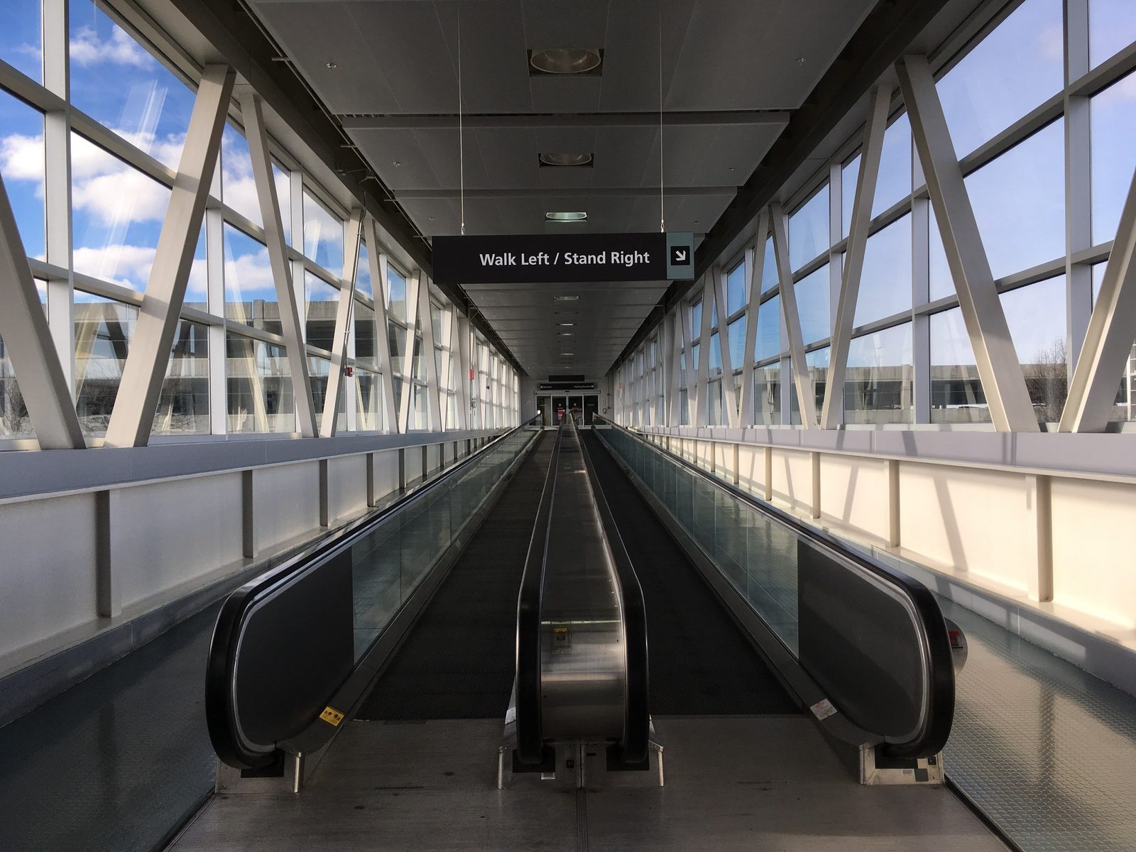 Interior photograph of a concourse corridor with a moving sidewalk, glass railings, and overhead lighting
